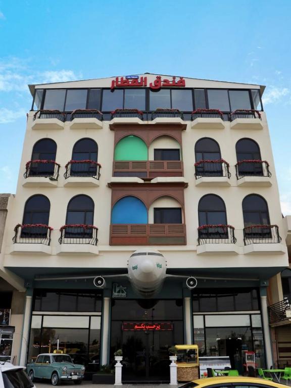 a large white building with windows and cars parked in front at Sky Airport Hotel - فندق سما المطار in Al Mawşil