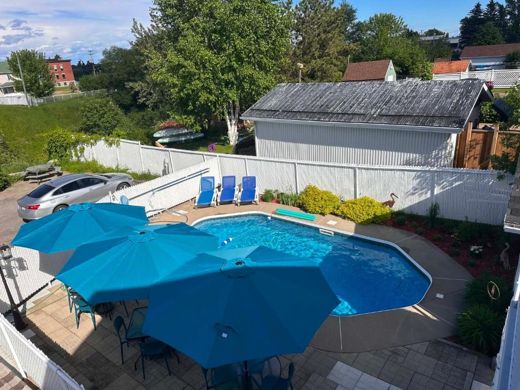 a swimming pool with blue umbrellas and chairs and a pool at Hôtel Auberge St-Félicien in Saint-Félicien