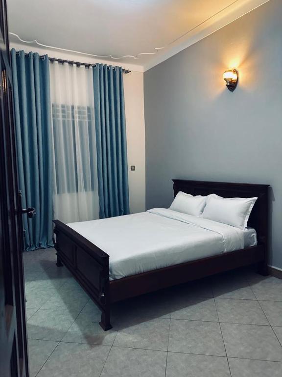 a bedroom with a large bed with blue curtains at Gugga Suites Mbale in Mbale