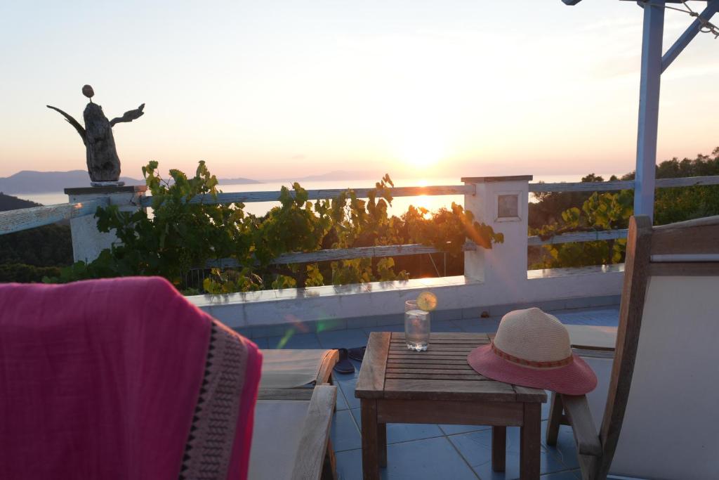 a table with a hat sitting on a balcony with the sunset at Villa Azul - A Timeless Retreat Above the Aegean in Alonnisos