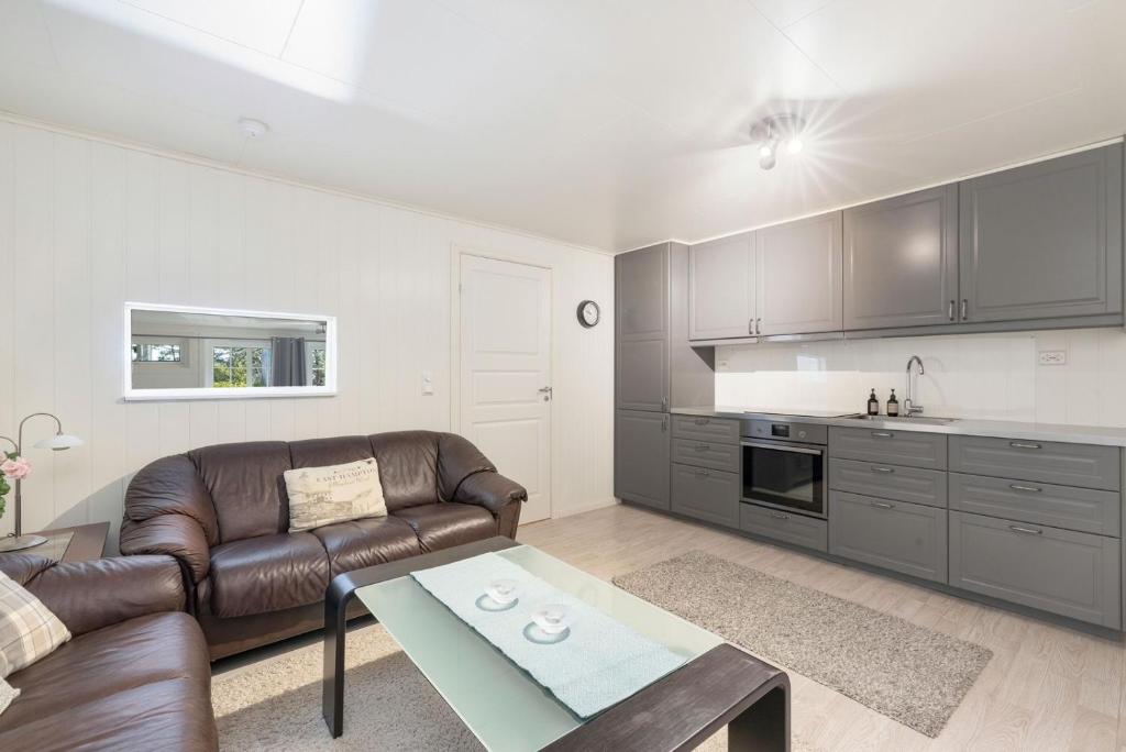 a living room with a leather couch and a kitchen at Nordic Stay in Grimstad