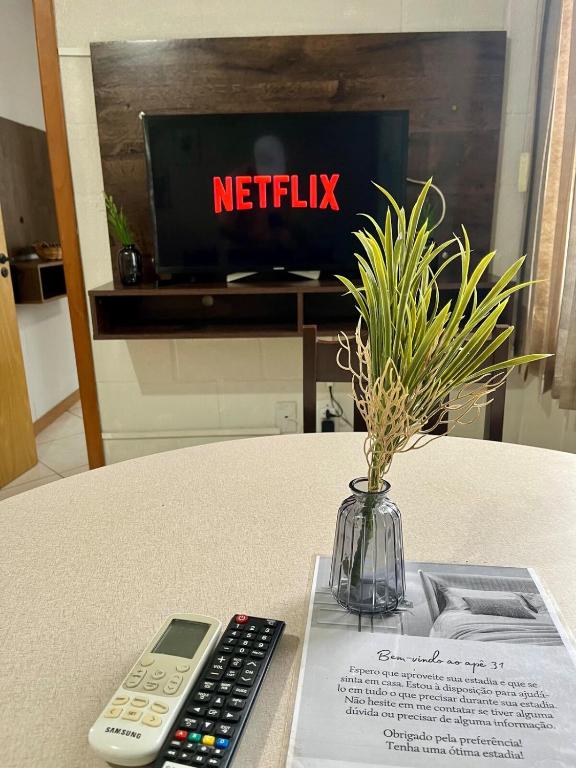 a remote control and a vase on a table with a tv at 08 - Apê próximo ao Metrô e Centro com Wi-Fi e Ar condionado in São Leopoldo