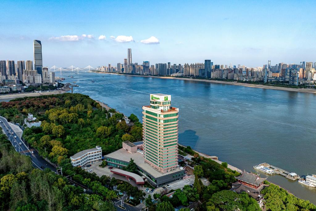 a tall building next to a river with a city at Holiday Inn Wuhan Riverside by IHG in Wuhan
