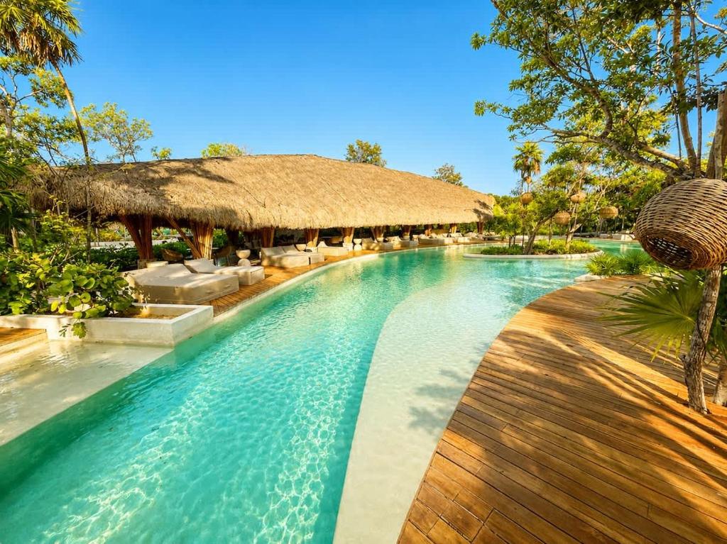 a swimming pool at a resort with a thatch roof at Mayan View Walk to Beach & Tulum Ruins in Tulum
