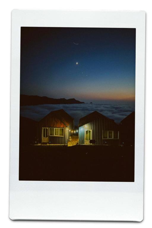 a view of two huts at night with the moon at Gomismta Golden Hour Cottages in Gomi