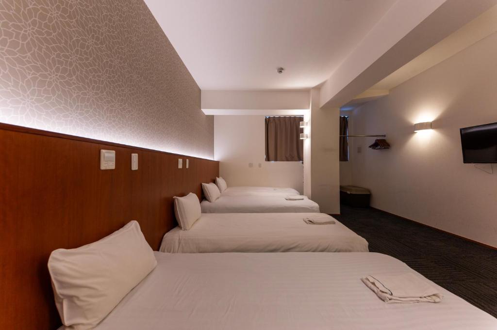 a hotel room with three beds and a tv at COCOSHUKU Tokyo Nakano in Tokyo