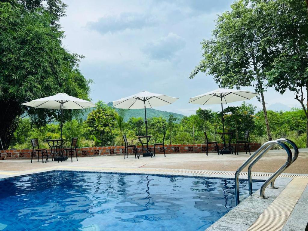 a pool with tables and chairs and umbrellas at Cloudy Hill Homestay and Hostel in Kampot
