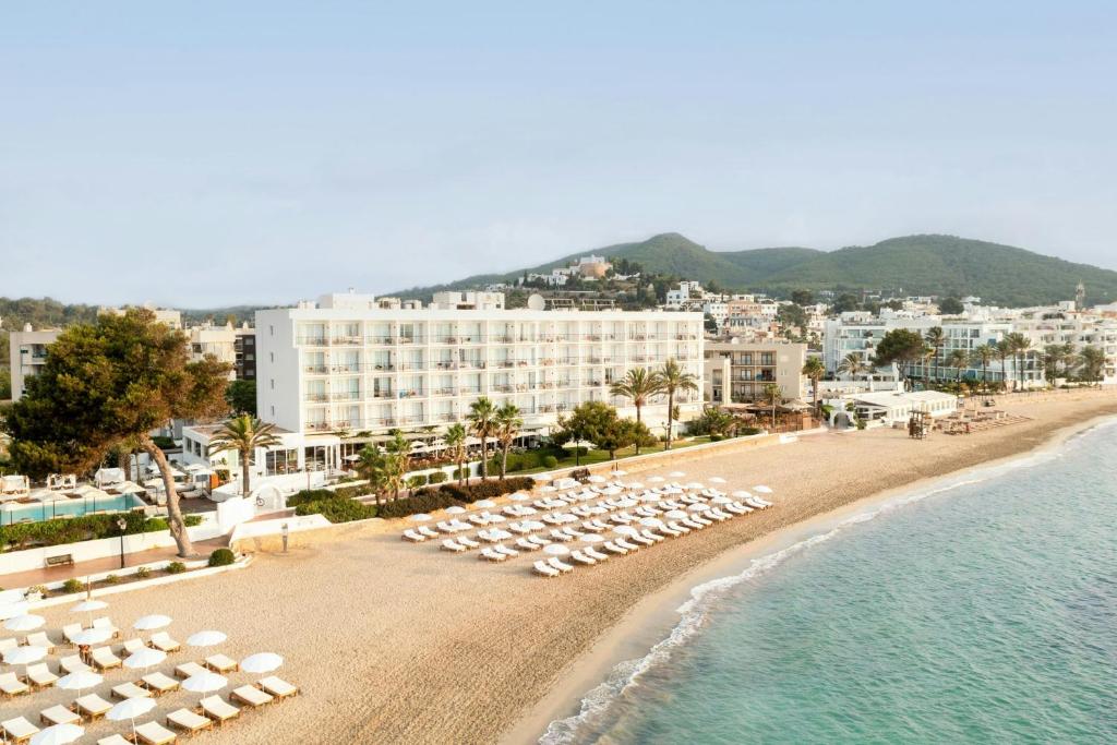 ein Strand mit Stühlen und Sonnenschirmen und ein Resort in der Unterkunft Hotel Riomar Ibiza, a Tribute Portfolio Hotel in Santa Eulària des Riu