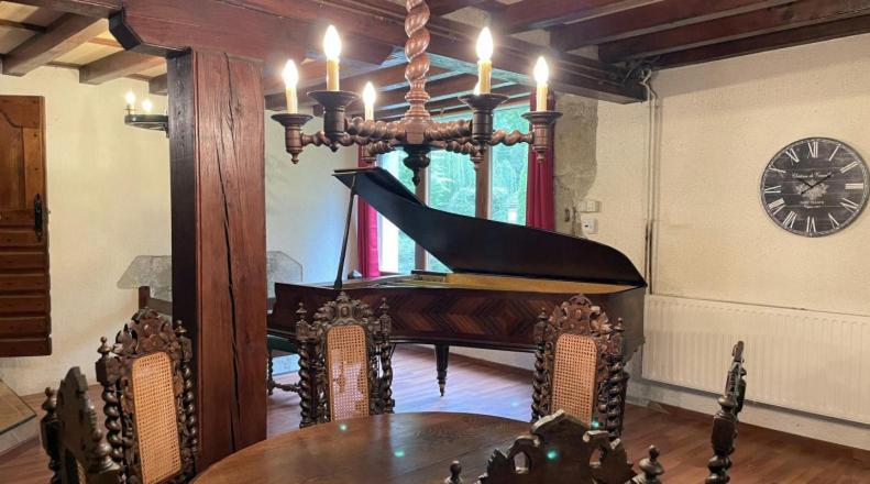 a piano in a room with a table and a clock at Gîte Le Pont du Soleil in Hyds