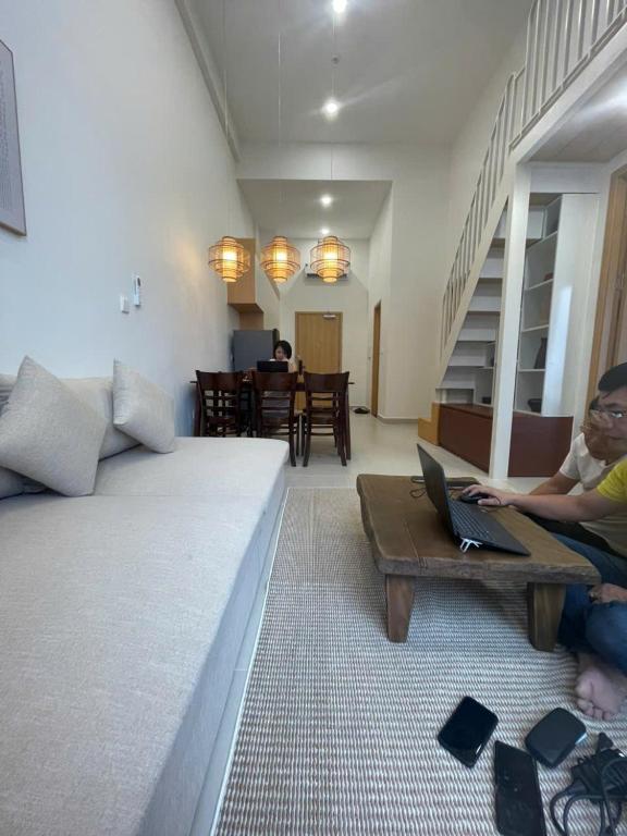 two people sitting in a living room with a laptop on a table at Sunora Stay A6 in Quang Ãm