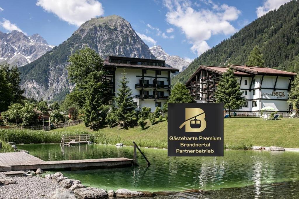 a sign in front of a building next to a lake at Alpenlodge - Das Dorfhotel in Brand