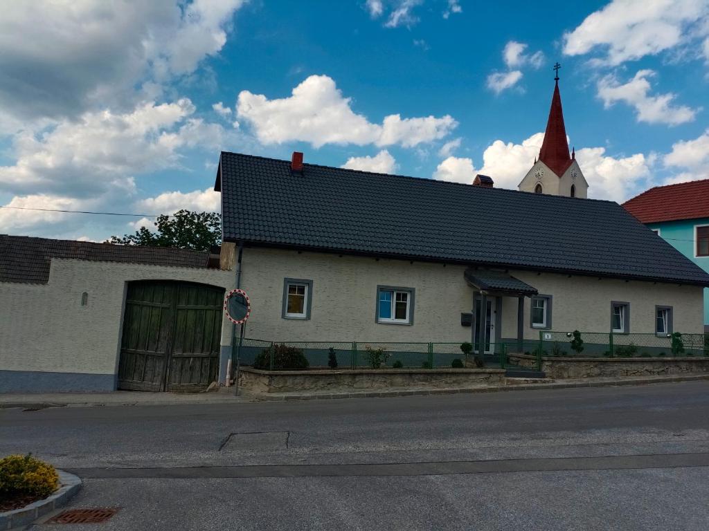a white building with a black roof and a church at Ferienhaus Strohmayer in Schweiggers