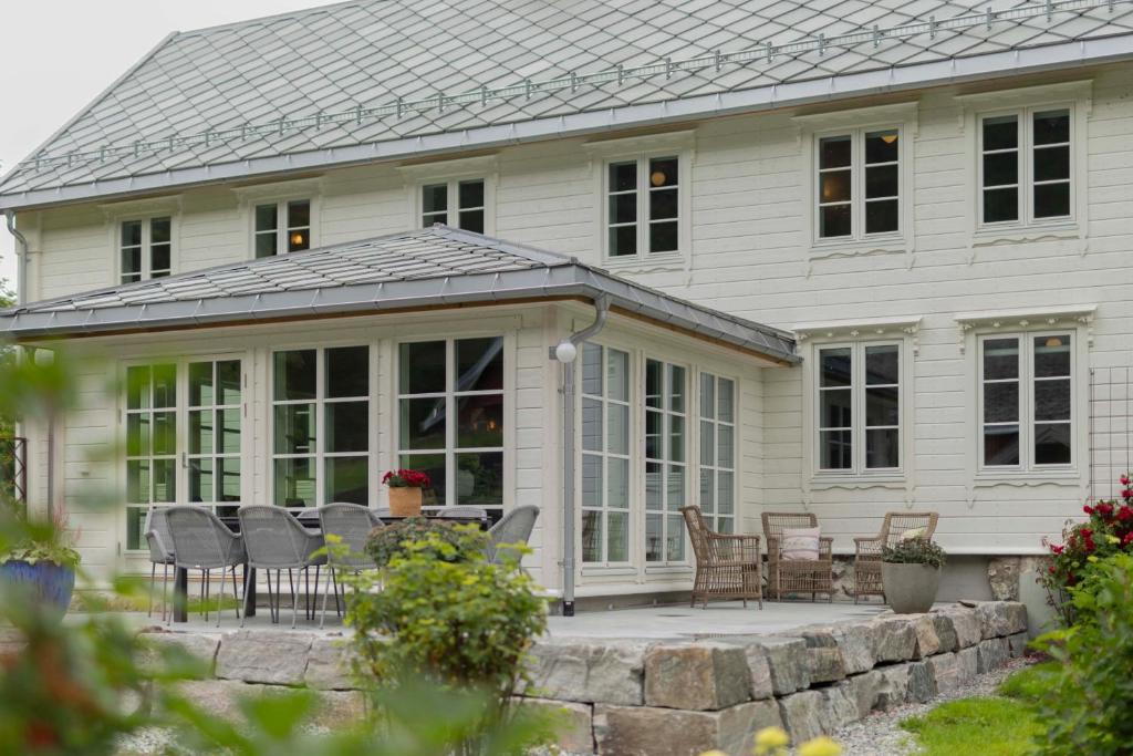 a white house with a patio with chairs and tables at Østigård 1810 Prestegårdshuset in Åndalsnes