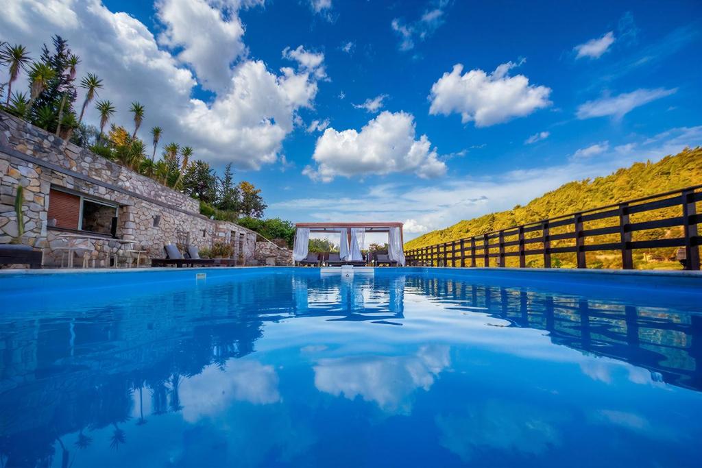 a swimming pool with a blue sky and clouds at Paxos Santa Marina Villas in Gaios