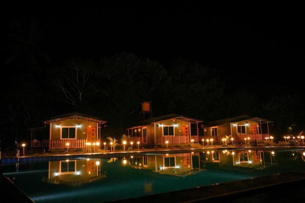 a couple of houses with lights around a swimming pool at night at Nature's Nook in Ganeshgudi