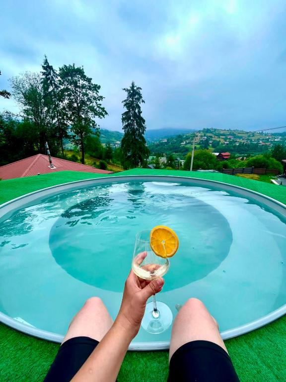 a person holding a drink in front of a swimming pool at Котедж Villagoria з теплим басейном in Slavske