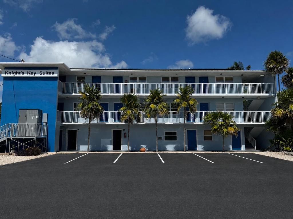 a large white building with palm trees in a parking lot at Knight's Key Suites in Marathon