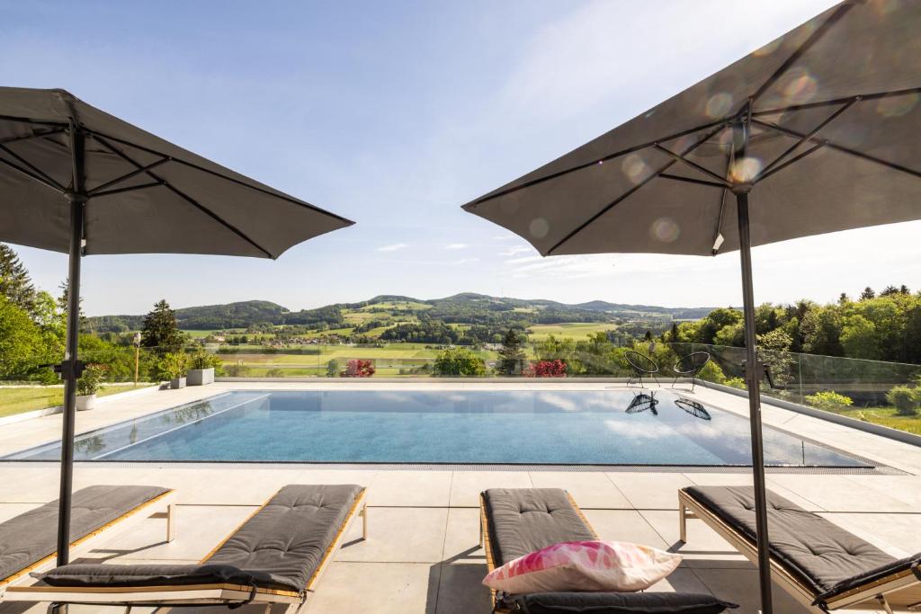 a swimming pool with chairs and umbrellas at Haus Vogl Anger - Ferienwohnungen mit privater Sauna und beheizten Salzwasser Pool in Panoramalage und Nähe zu Salzburg und Berchtesgaden in Anger