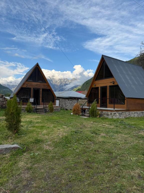 two large wooden buildings with mountains in the background at Twenty 23 Cottages,kazbegi 1 in Kazbegi