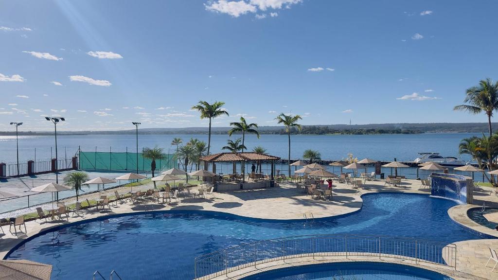 a large swimming pool with umbrellas and a body of water at Flat 337 vista lago no Lake side in Brasília