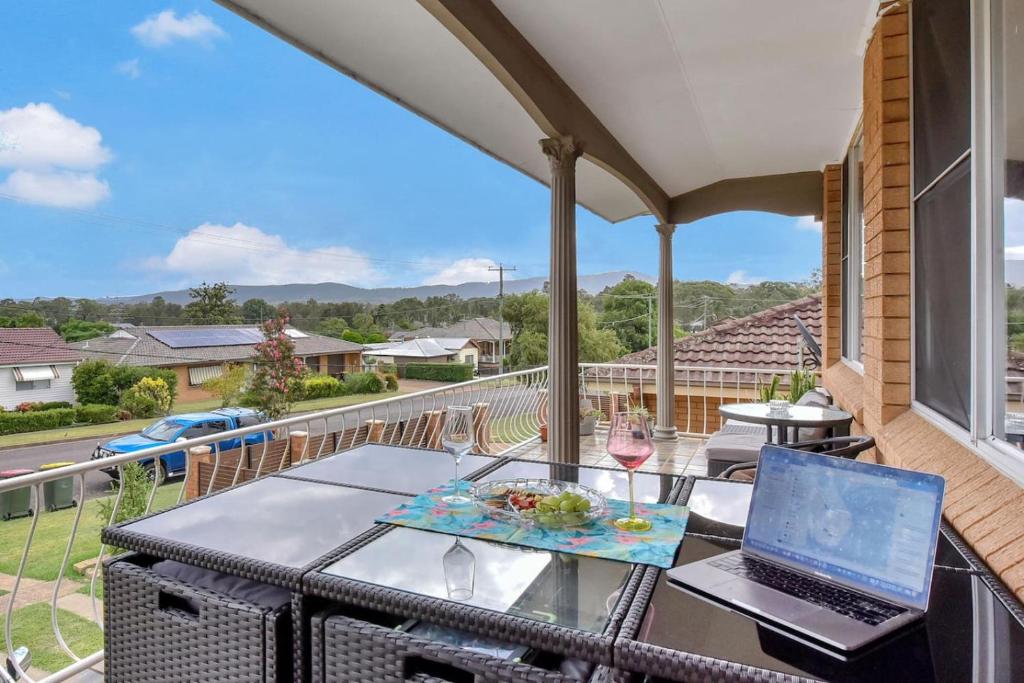 a balcony with a table with a laptop and wine glasses at Coal d' Vine VIEW - Cessnock NSW in Cessnock