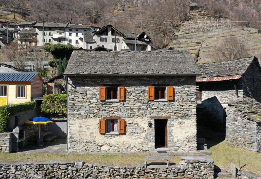 ein altes Steinhaus mit orangefarbenen Türen auf einem Hügel in der Unterkunft Rustico Scoperta in Linescio