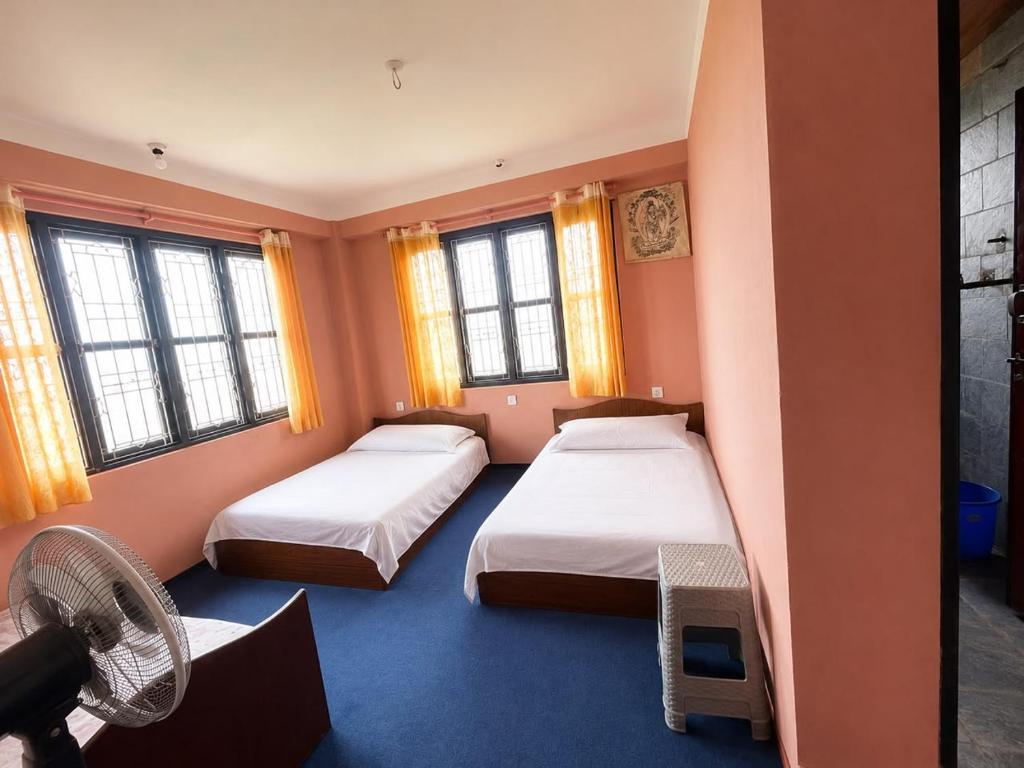 a room with two beds and a fan and windows at Hilltop Horizon Hotel in Bandipur
