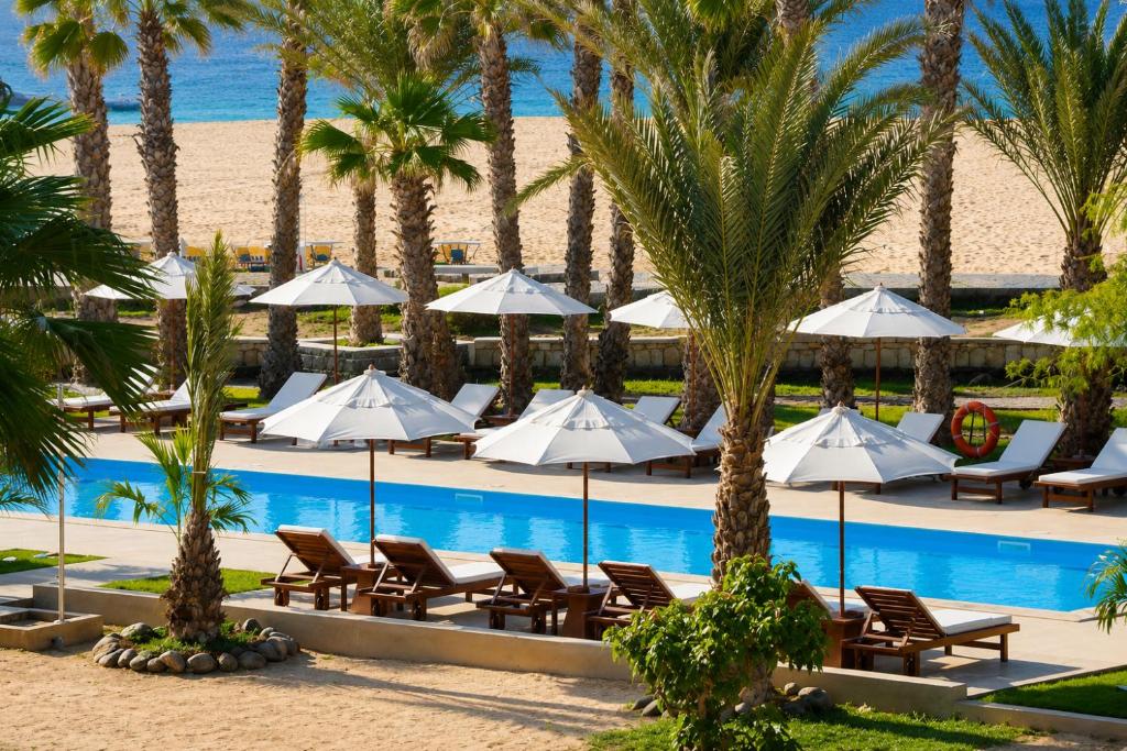 a resort pool with chairs and umbrellas and palm trees at Hotel Morabeza in Santa Maria