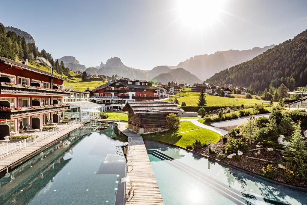 a village with a river and mountains in the background at Hotel Alpenroyal - The Leading Hotels of the World in Selva di Val Gardena