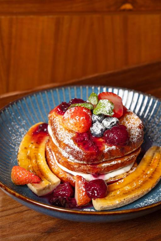 Stacked pancakes with berries, banana and powdered sugar fill a blue ceramic plate.