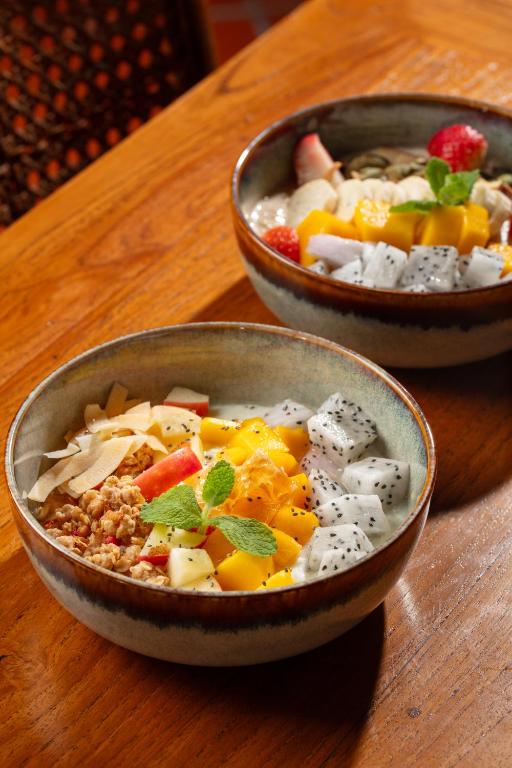 Two colorful fruit-and-granola bowls are served on a wooden breakfast table.