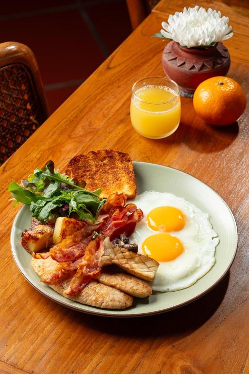 A full cooked breakfast with eggs, bacon, sausages, toast, potatoes, greens and juice.