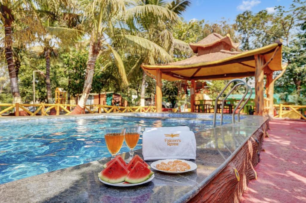 a table with two glasses of juice and food next to a swimming pool at Falcon's Retreat in Pune