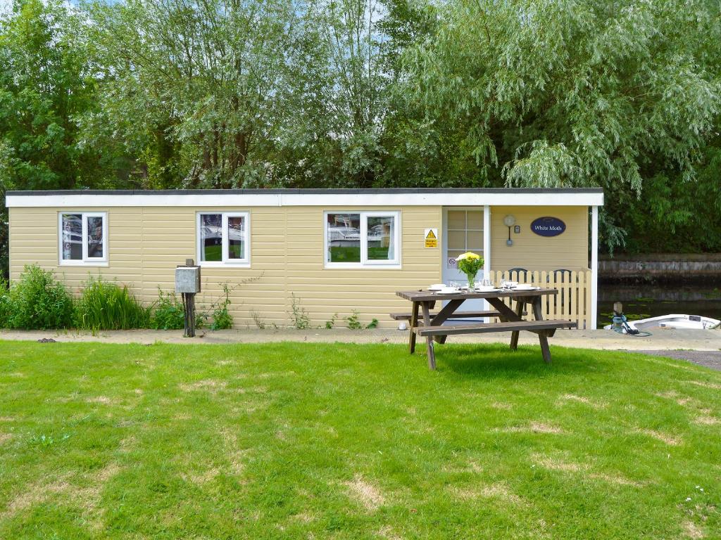 a small yellow caravan with a picnic table in a yard at White Moth - Uk12697 in Stalham