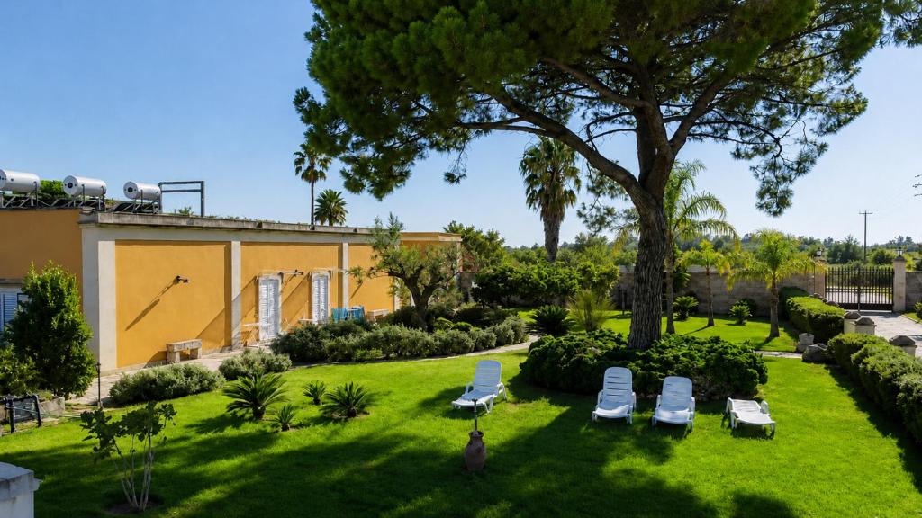 a lawn with chairs and a tree and a building at Tenuta Masseria del Gallo in Calimera
