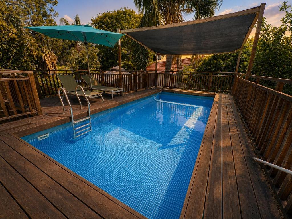 a pool with an umbrella and a chair and a table at אתנחתא בירדן in Mishmār Hāyardin