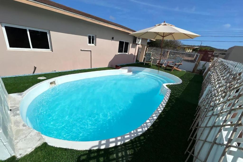 a swimming pool with an umbrella next to a house at Hidden Gem Savaneta & Private Pool in Savaneta