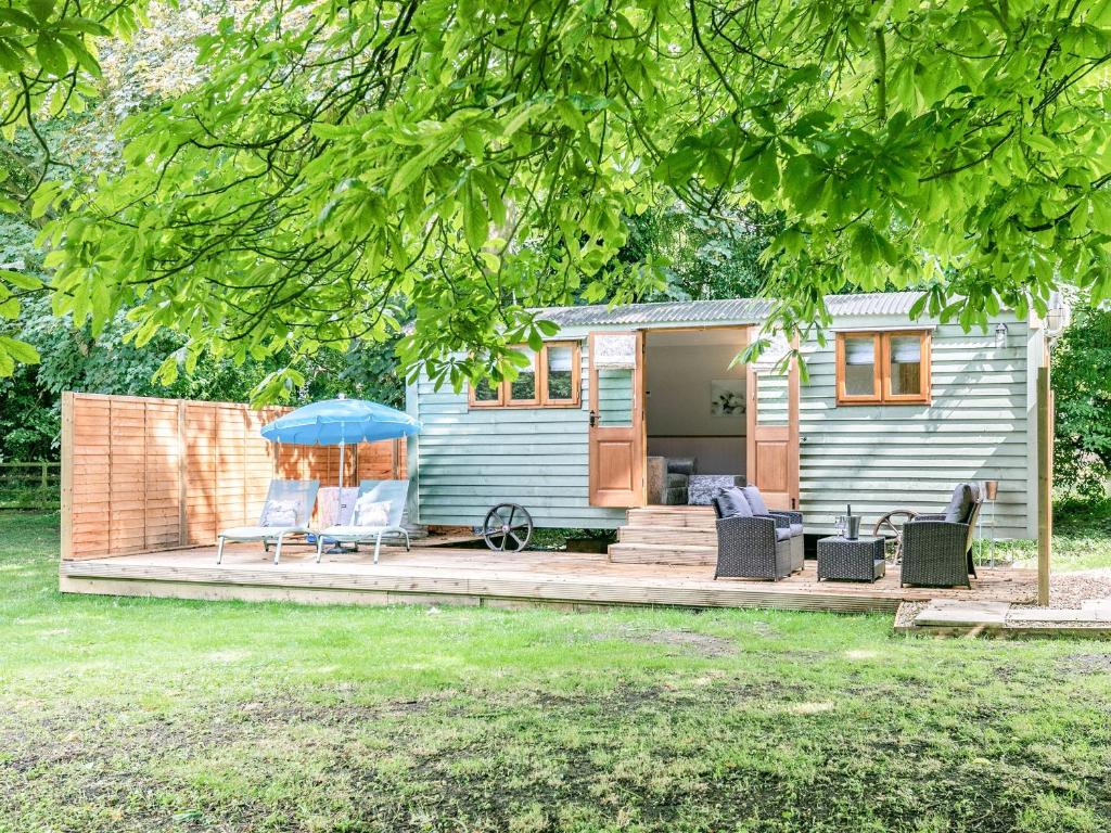 a blue tiny house with chairs and an umbrella at Snow Drop Hut in Alkborough