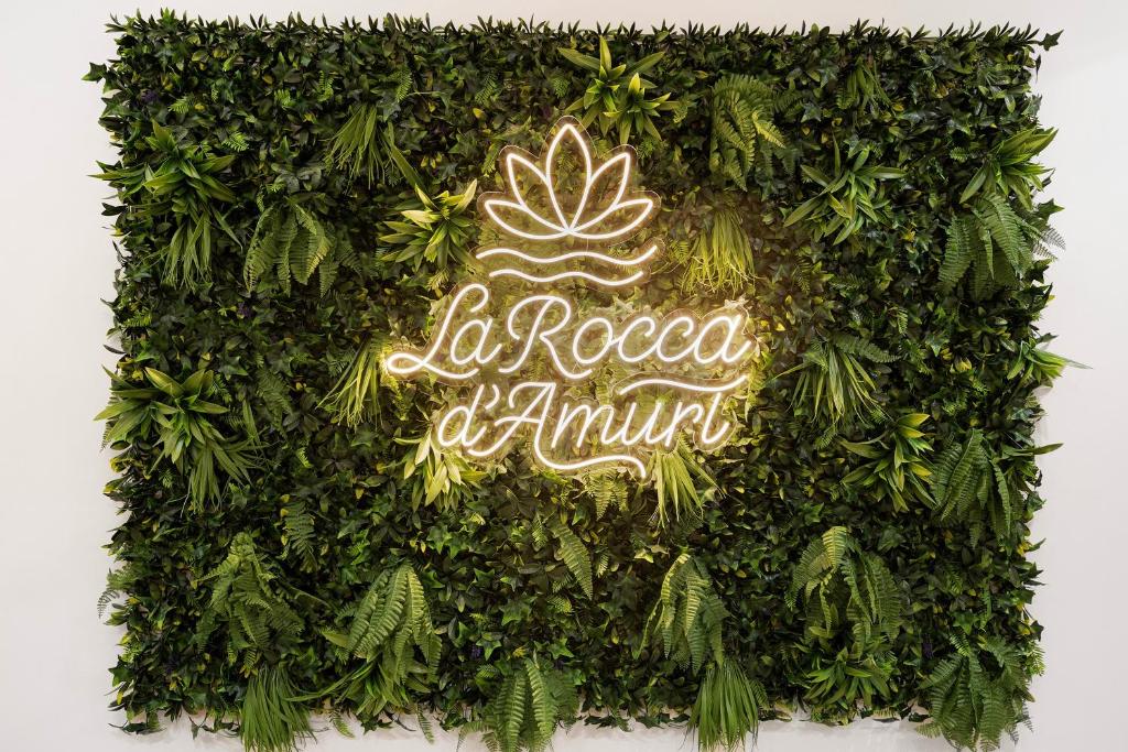 a green hedge with a sign that reads be rooted at anytime at La Rocca D’Amuri in Partinico