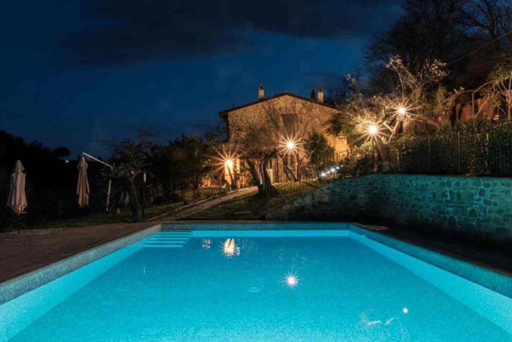 a blue swimming pool in front of a house at night at Le Case Gialle Resort in Gualdo Cattaneo