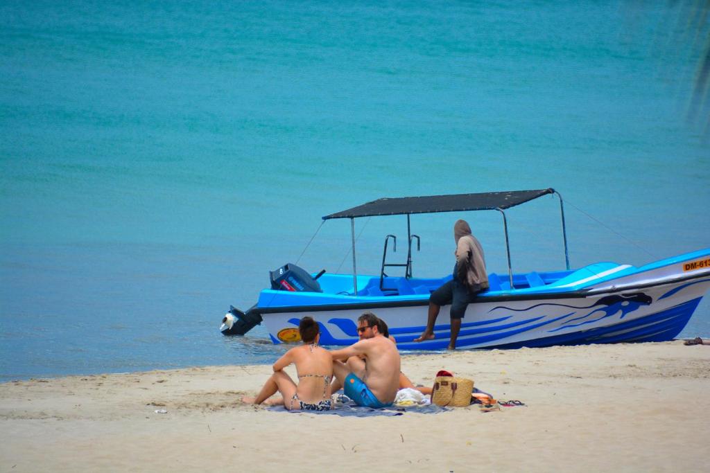 a group of people sitting on the beach next to a boat at Trinco Eddi Resort in Trincomalee