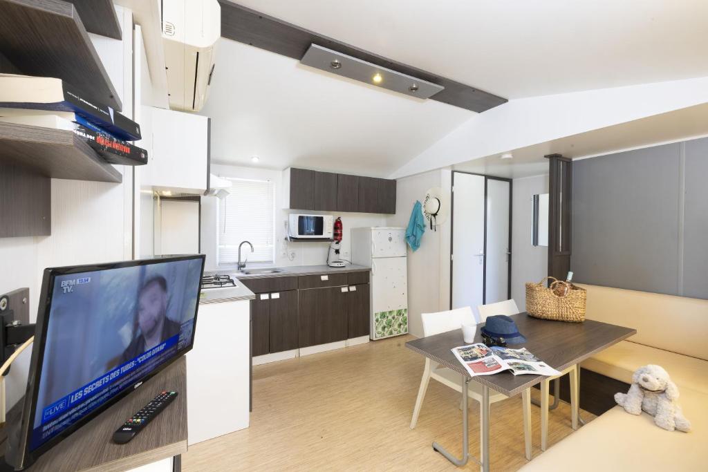 a living room with a tv and a table and a kitchen at Camping Les Nysades in Mirepoix