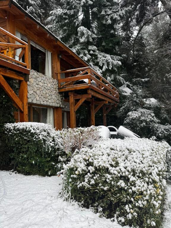 a house with snow on the ground next to some bushes at El Remanso del Lago in Villa La Angostura