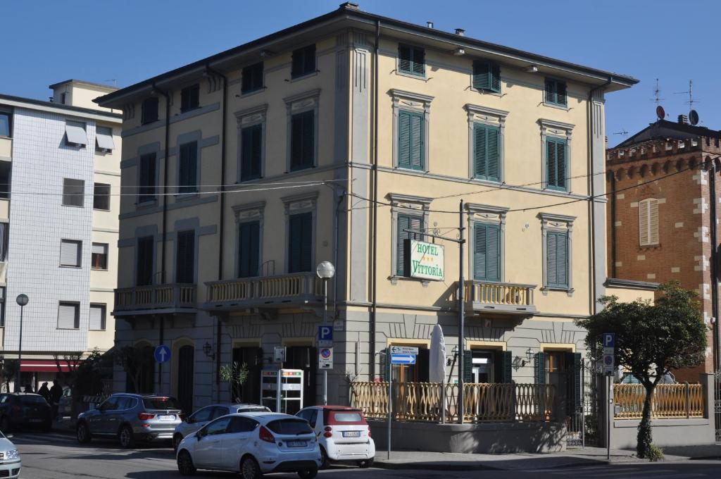 un gran edificio con coches estacionados frente a él en Hotel Vittoria, en Viareggio