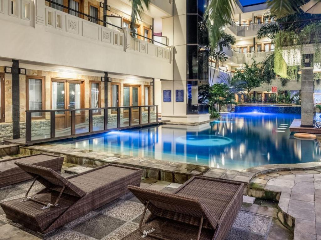 a large swimming pool in a building with two chairs at Famous Hotel Kuta Formerly Permata Kuta Hotel in Kuta