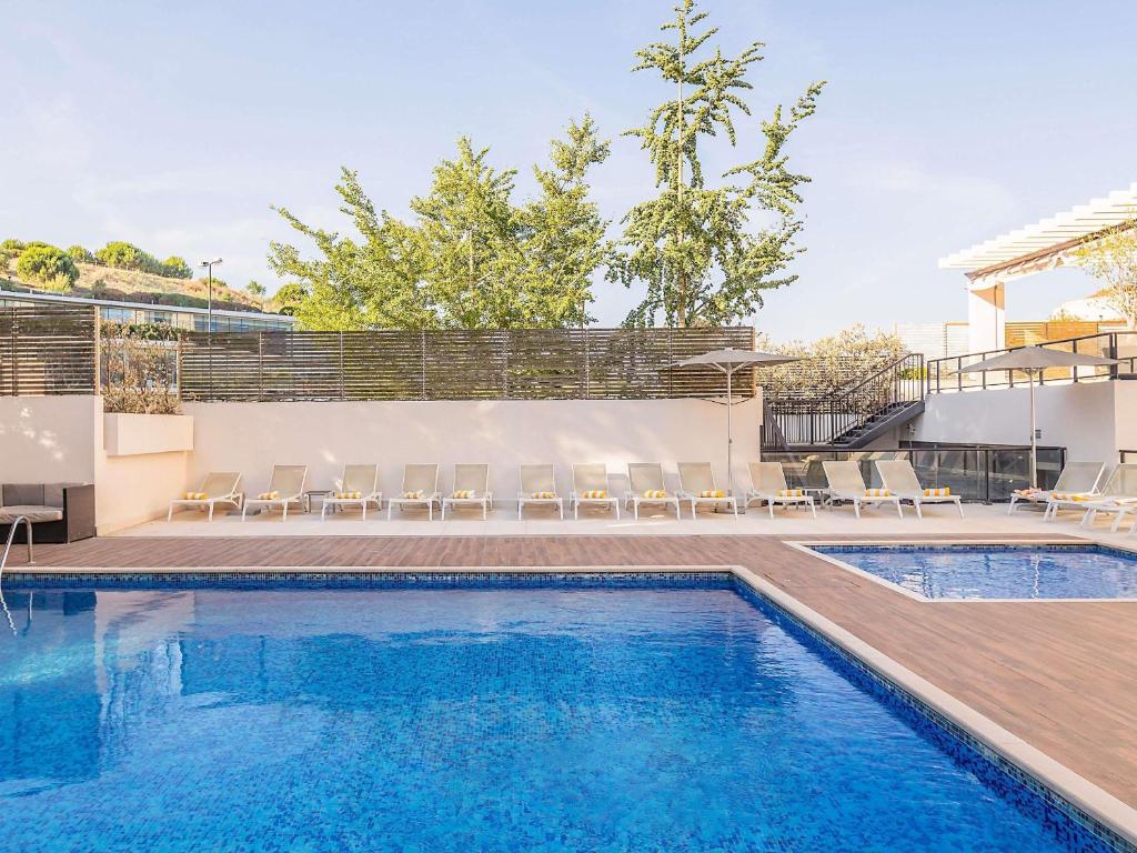a swimming pool with a deck and chairs next to a house at Novotel Lisboa in Lisbon