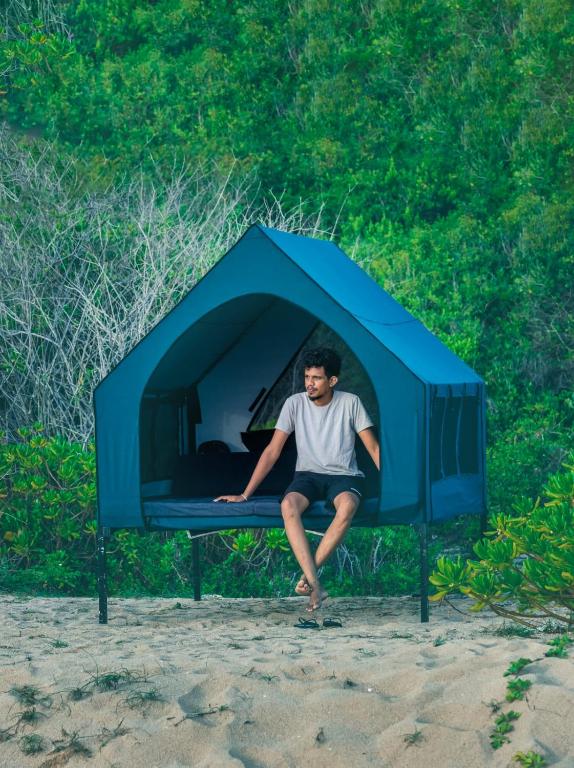 a man sitting on a bed in a tent at Kuma Surf Camp in Arugam Bay