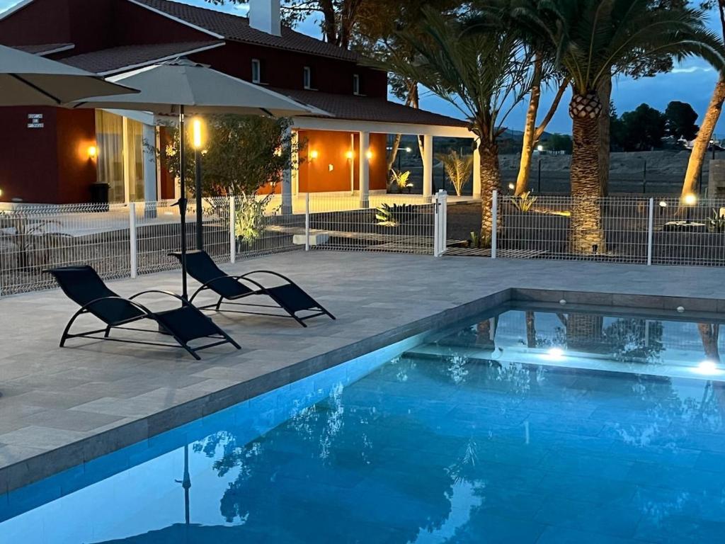 a swimming pool with two chairs and an umbrella at Cortijo el Viznagar in Las Casicas