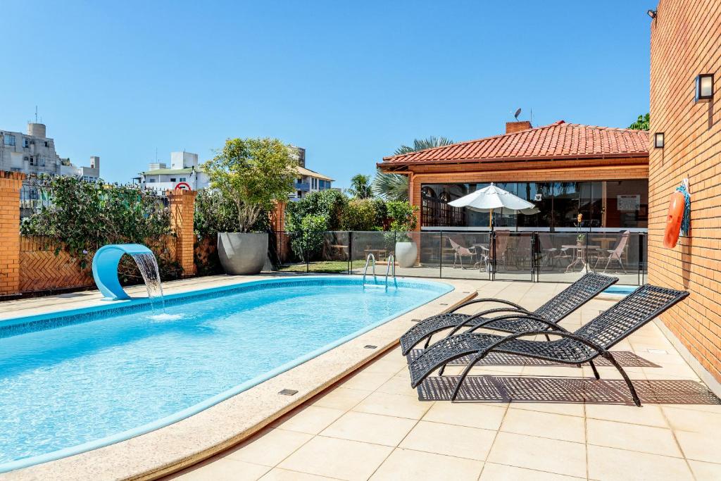 a swimming pool with two chairs and an umbrella at Elite Hotel in Florianópolis
