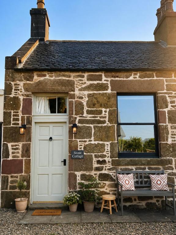 a stone cottage with a white door and a bench at Stone Cottage Relax & Unwind, Cosy Cinema Retreat in Laurencekirk